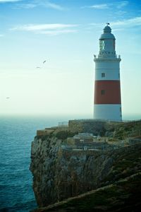 Lighthouse by sea against buildings