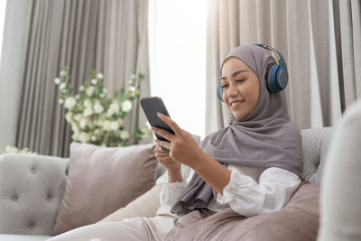 Young woman using mobile phone while sitting on sofa at home