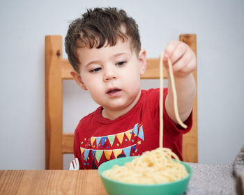 Cute boy is playing with his pasta at lunch time