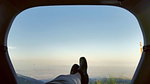 Low section of man on airplane window against clear sky