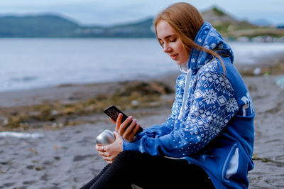 Young woman using phone while sitting at beach