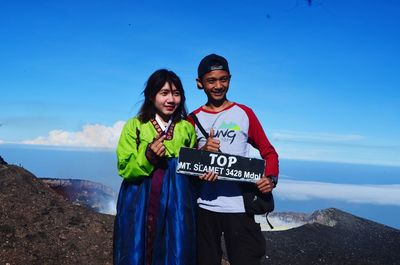 Portrait of smiling young couple standing on mountain against sky
