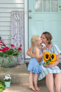 Woman and girl holding flower while standing by building