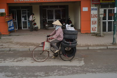 Rear view of man riding bicycle on street against building