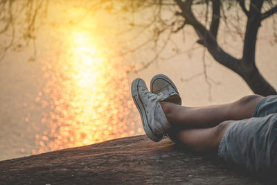 Low section of woman standing on tree during sunset