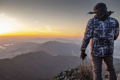 Rear view of man looking at mountains against sky during sunset