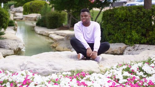 Full length portrait of young man sitting on rock