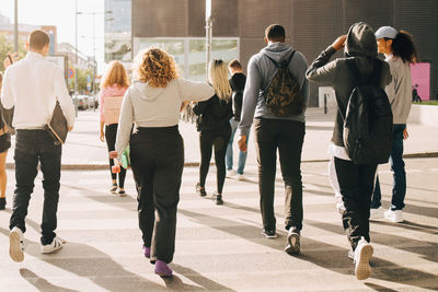 Rear view of friends crossing street in city during sunny day