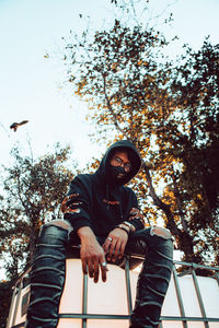 Portrait of young man sitting on plant against trees