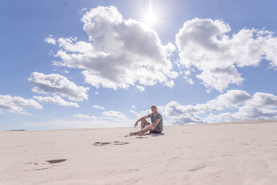 Man sitting on sand dune in desert against sky