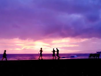 Silhouette people playing on beach against sky during sunset