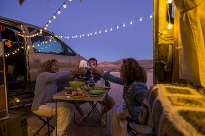 Cheerful people toasting wine while siting by van against sky