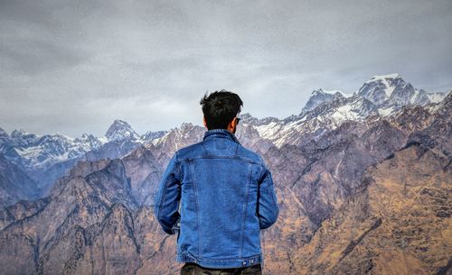 Rear view of man standing on mountain against sky