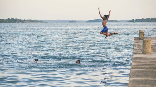 Friends looking at boys diving into sea against clear sky