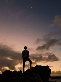 Silhouette man standing on rock against sky during sunset