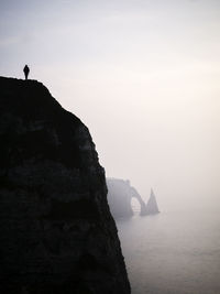 Silhouette cliff by sea against sky