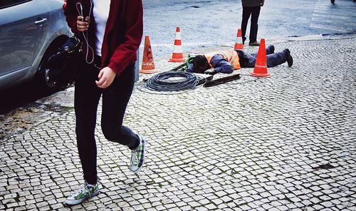 Manual worker working at sewage while woman walking on cobbled sidewalk