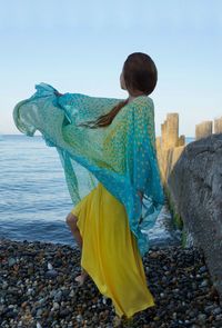 Woman standing on rock by sea against sky