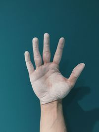 Close-up of cropped dusty hand against blue background