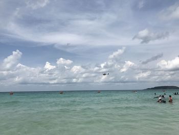 People in sea against cloudy sky