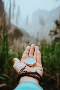 Cropped hand of woman holding navigational compass against trees