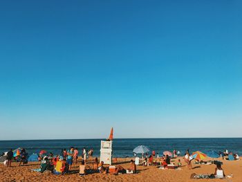 People at beach against clear blue sky