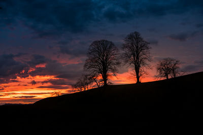 Silhouette bare trees against dramatic sky during sunset