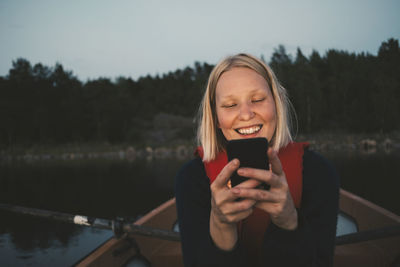 Smiling woman using mobile phone while sitting in boat on lake