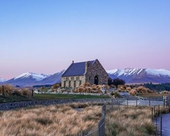 Houses on field by snowcapped mountains against clear blue sky