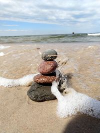 Stack of pebbles on sand at beach against sky