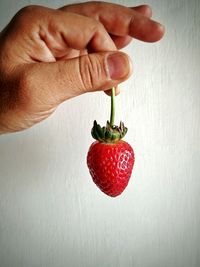 Close-up of hand holding strawberry over white background