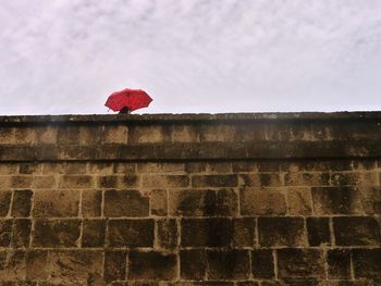 Low angle view of woman carrying red umbrella by railing during rainy season