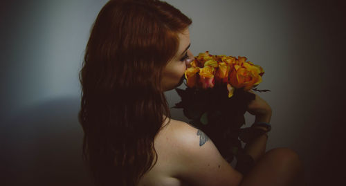 Naked young woman holding rose bouquet against gray wall