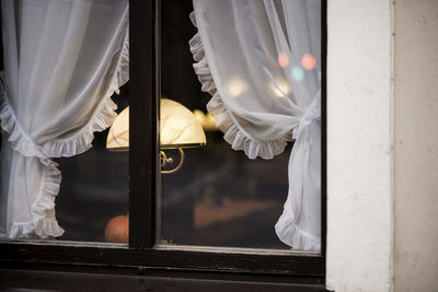 Illuminated lamp and white curtains behind closed window