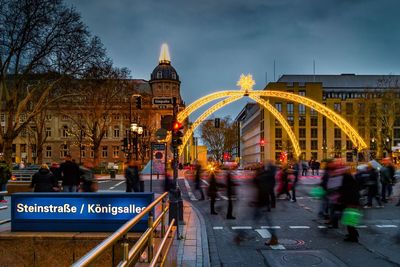 Blurred motion of people walking on road against sky in city