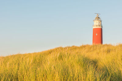 Lighthouse on field by building against clear sky