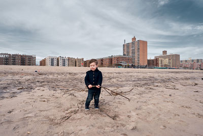 Happy young toddler running around the beach with a big branch