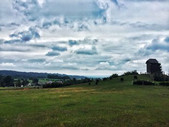 Houses on grassy field against cloudy sky