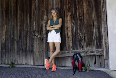 Happy senior woman wearing orange shoes with arms crossed leaning on old wooden barn door