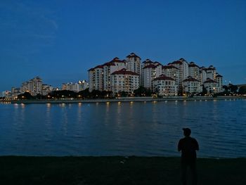 Rear view of illuminated buildings by sea against clear blue sky