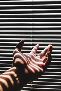 Cropped hand of person gesturing by window blinds