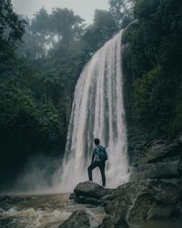 Man surfing on rock against waterfall