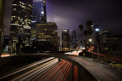 Light trails on road amidst illuminated buildings in city at night