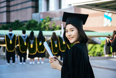 Young woman wearing black graduation gown standing in city