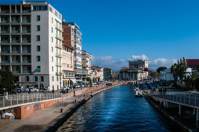 Canal amidst buildings against blue sky