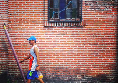 Side view of boy standing against brick wall