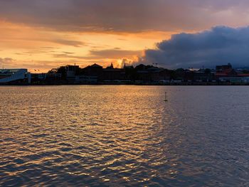 Sea by buildings against sky during sunset