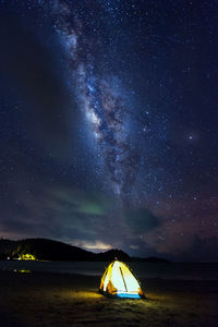 Illuminated tent at beach against sky at night