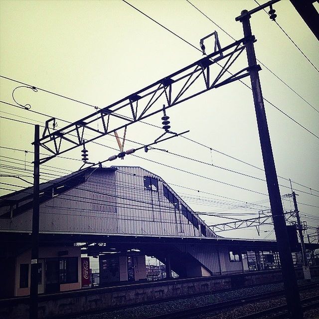 power line, architecture, built structure, cable, connection, electricity pylon, building exterior, transportation, railroad track, rail transportation, power supply, railroad station, low angle view, sky, electricity, clear sky, public transportation, railroad station platform, train - vehicle, power cable