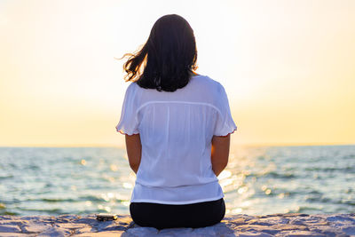 Rear view of woman on sea shore against sky during sunset